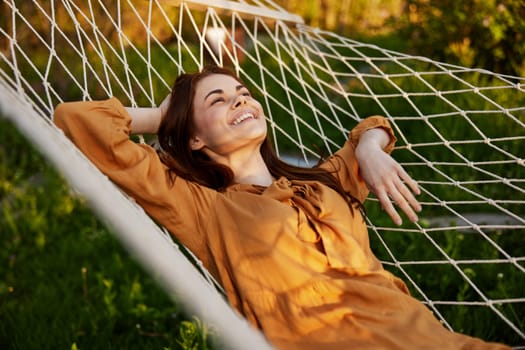 a happy woman is resting in a hammock with her eyes closed and her hands behind her head smiling happily enjoying the day. High quality photo