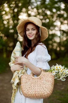 a woman with a wicker hat, a bag and a plaid smiles while standing in nature in the park. High quality photo