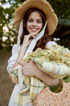 a woman with a wicker hat, a bag and a plaid smiles while standing in nature in the park. High quality photo