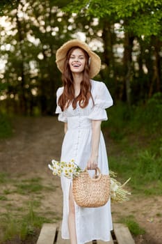 joyful woman in a wicker hat and with a basket in her hands stands in nature