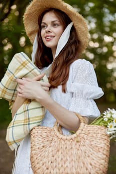 a woman with a wicker hat, a bag and a plaid smiles while standing in nature in the park. High quality photo