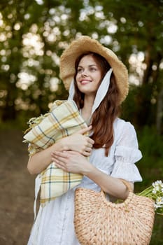 a woman with a wicker hat, a bag and a plaid smiles while standing in nature in the park. High quality photo