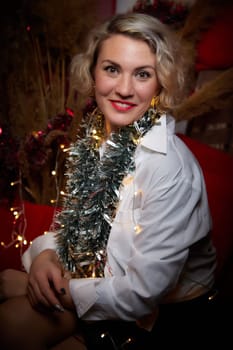 Portrait of a beautiful laughing funny blonde girl with light of garland on dark background before Christmas or New Year