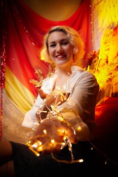 Portrait of a beautiful laughing funny blonde girl with light of garland on dark background before Christmas or New Year