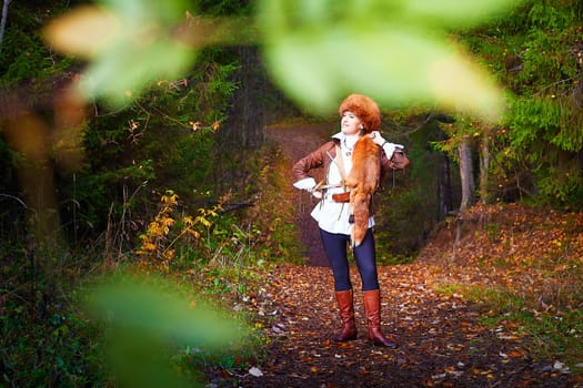 Girl in a leather jacket, a big red fox fur hat and with the skin of a fox killed on the hunt in the forest in autumn. A female model poses as fabulous royal huntress on nature hunt at photo shoot