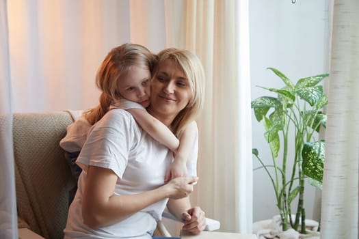 Happy loving family with mother and daughter having hugs in living room. Woman mom and small child girl inside of home