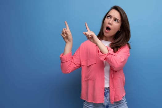 shocked black haired lady in casual style pointing finger at wall in studio background.