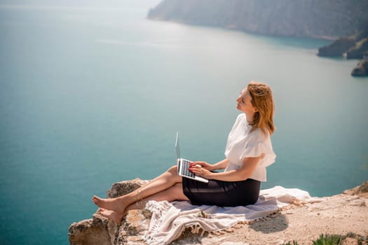 Freelance woman working on a laptop by the sea, typing away on the keyboard while enjoying the beautiful view, highlighting the idea of remote work