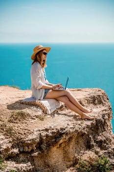 Freelance woman working on a laptop by the sea, typing away on the keyboard while enjoying the beautiful view, highlighting the idea of remote work