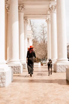 A photo of a woman and her Great Dane walking through a town, taking in the sights and sounds of the urban environment.