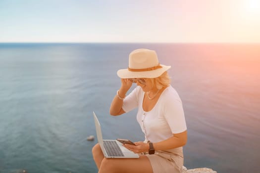 Freelance women sea working on the computer. Good looking middle aged woman typing on a laptop keyboard outdoors with a beautiful sea view. The concept of remote work