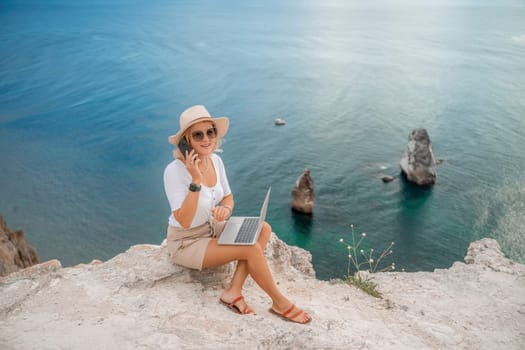 Freelance women sea working on the computer. Good looking middle aged woman typing on a laptop keyboard outdoors with a beautiful sea view. The concept of remote work