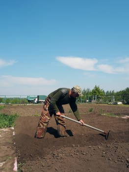 The concept of private agriculture.An elderly pensioner works with a hoe on the ground for planting vegetables.Spring sowing work.