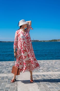 woman in a hat and dress enjoys the blue sea and summer. Welcome summer