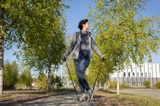 Fitness Walking With Two Sticks. Happy Caucasian Woman Training In Urban Park, Forest. Physical Activity, Pole Walking. Sports Tourism, Outdoor Recreation. Lifestyle. Horizontal Plane.