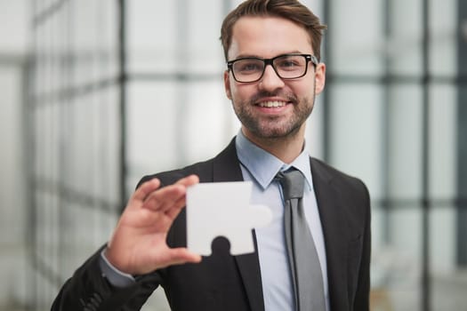 Portrait of an optimistic businessman holding puzzle pieces, solving problems, looking at the camera, wearing a black suit.