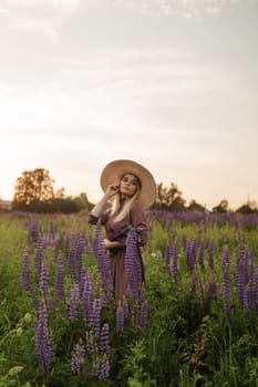 A beautiful woman in a straw hat walks in a field with purple flowers. A walk in nature in the lupin field.