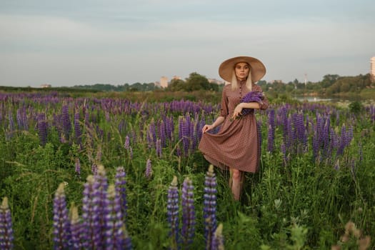 A beautiful woman in a straw hat walks in a field with purple flowers. A walk in nature in the lupin field.