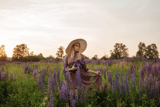 A beautiful woman in a straw hat walks in a field with purple flowers. A walk in nature in the lupin field.