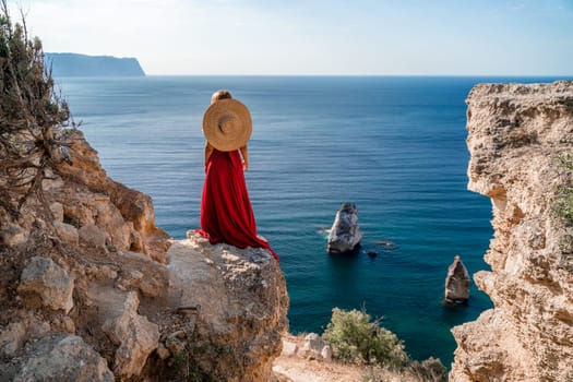 A woman in a flying red dress fluttering in the wind and a straw hat against the backdrop of the sea