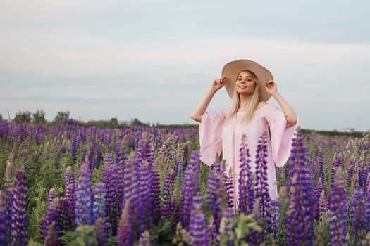 A beautiful woman in a straw hat walks in a field with purple flowers. A walk in nature in the lupin field.