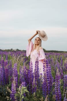 A beautiful woman in a straw hat walks in a field with purple flowers. A walk in nature in the lupin field.