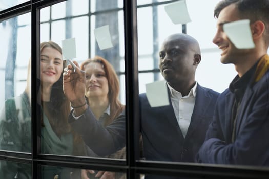Creative business team looking at sticky notes on glass window