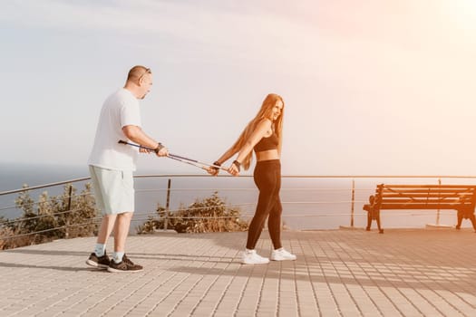 Happy Middle aged couple or friends practicing nordic walking in park near sea. Mature couple with trekking poles walking, practicing Nordic walking outdoors. Aging youthfully and sport concept.