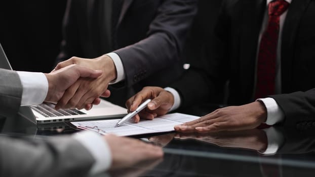 businessmen shaking hands, cooperation in the office and financial paper graphics on the table