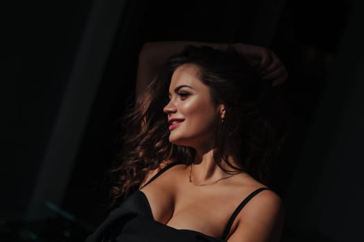 Portrait of a sexy brunette in a black dress on a dark background. girl takes off her dress slowly in the bedroom.