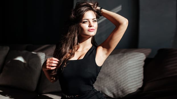 Portrait of a sexy brunette in a black dress on a dark background. girl takes off her dress slowly in the bedroom.