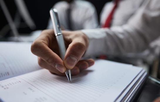 Businessman hand writing note on a notebook close-up. Business man working at office desk.