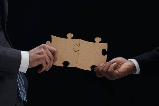 Close-up Of Business Partners Combining Two White Puzzle Pieces On Black Background