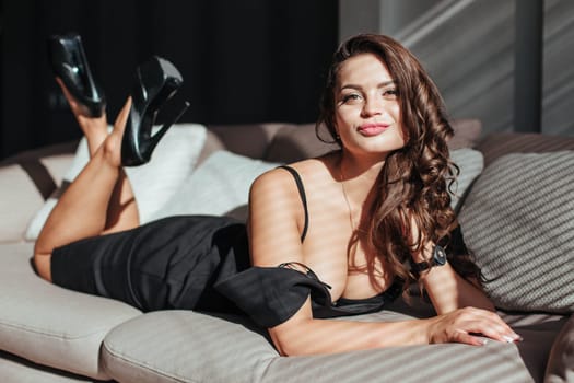 Portrait of a sexy brunette in a black dress on a dark background. girl takes off her dress slowly in the bedroom.