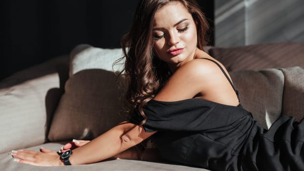 Portrait of a sexy brunette in a black dress on a dark background. girl takes off her dress slowly in the bedroom.