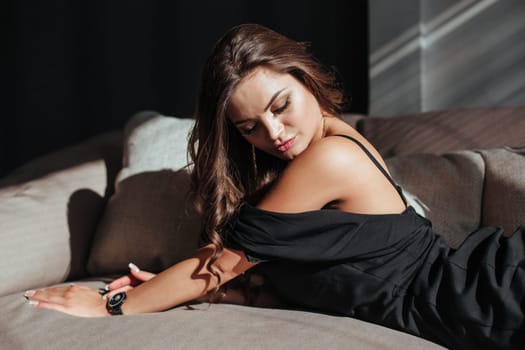 Portrait of a sexy brunette in a black dress on a dark background. girl takes off her dress slowly in the bedroom.