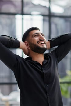 Portrait of relaxed businessman in modern office.Business young man relax after work of office window with business district view.