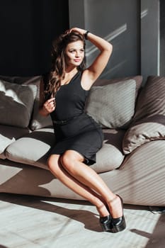 Portrait of a sexy brunette in a black dress on a dark background. girl takes off her dress slowly in the bedroom.