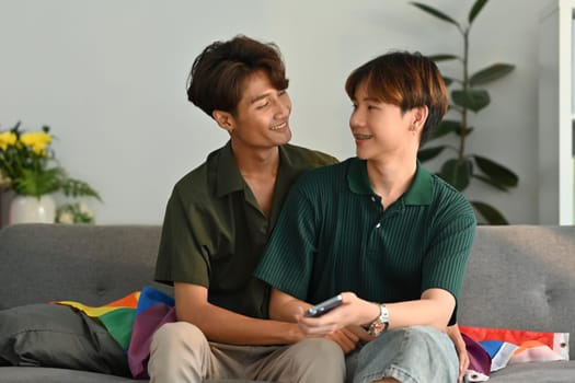 Cheerful two men couple using smartphone, relaxing on couch at home. LGBT, love and lifestyle relationship concept.