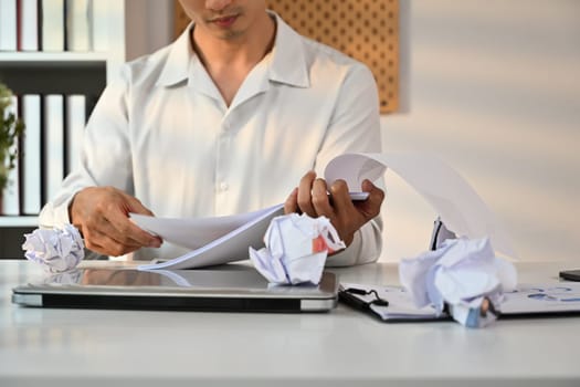 Cropped sot of male entrepreneur working with account documents at white office desk with crumped paper.
