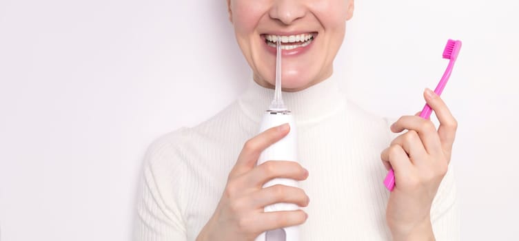 Cropped smiling with ideal teeth woman holds oral irrigator, toothbrush on white background.Caucasian girl keeps white healthy teeth with oral cleaning,flossing,brushing.Dentistry,dental care concept