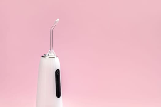 Cropped Oral teeth irrigator, dental water tooth cleaner, white portable rechargeable cordless water dental flosser on pink background. Waterproof home dental care device with nozzle.Horizontal