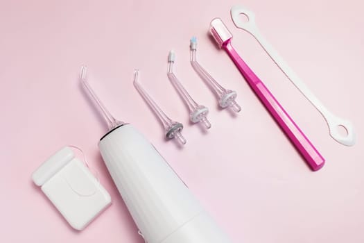 Oral hygiene set. Oral teeth irrigator with nozzle pack, toothbrush, dental floss, tongue scraper. Top view, pink background Dental care, treatments, daily routine. Horizontal plane, closeup