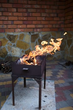 Still life with branches burning in flaming fire in barbecue grill. Preparation of food in the open air in the backyard against a red brick wall background. The season of summer picnic and BBQ party