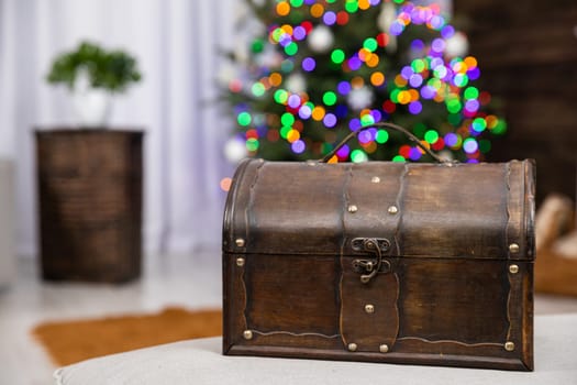A decorative old trunk made of wood stands in the foreground. The second plan with a fuzzy Christmas tree with Christmas tree lights lit.