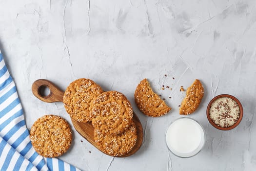 Oatmeal cookies with sesame seeds and flax seeds on a gray background with a jar of oatmeal and a glass of milk.Copy space