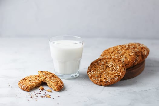 Oatmeal cookies with sesame seeds and flax seeds with a glass of milk on a gray background.