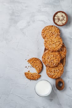 Oatmeal cookies with sesame seeds and flax seeds on a gray background with a jar of oatmeal and a glass of milk.Copy space