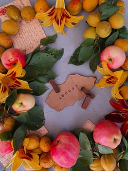 Autumn apples, apricots, yellow flowers are laid out on a gray background and the inscription August is written.