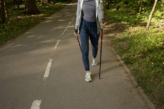 Cropped Female Legs Trekking With Sticks, Step Along The Path In Park, Cropped Hiking Female, Nordic Walking With Sticks, Cross-country Running. Horizontal Plane. CopySpace For Text.High quality photo